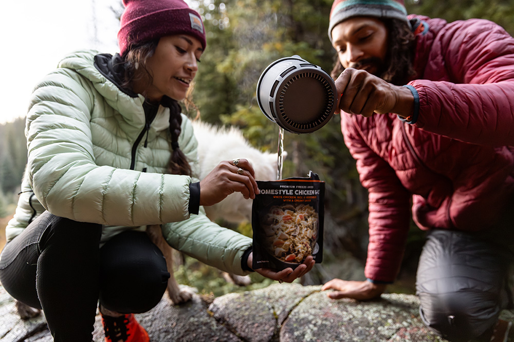 Two campers pour hot water into a dehydrated backpacking meal.