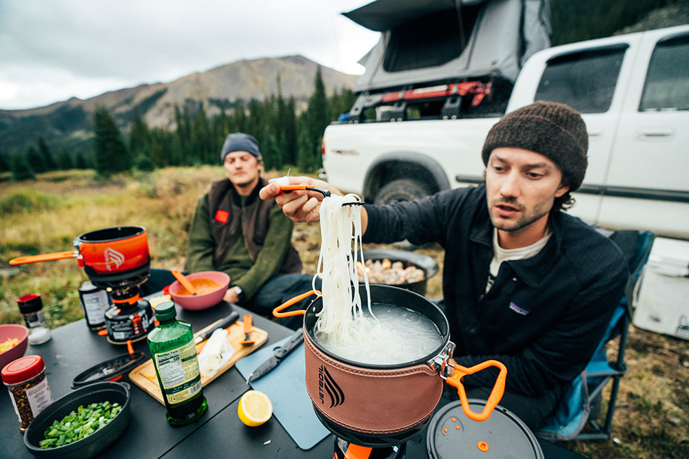 Man lifting cooked noodles out of Jetboil TrailCook 2.0L Cooking system with Trailware Fork during a car camping trip 