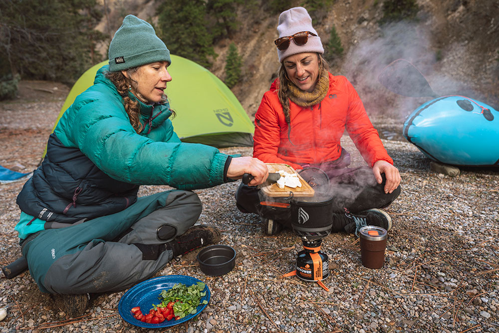 Two women at hiking campsite adding protein to boiling water in the Jetboil TrailCook 1.2L cooking system adding
