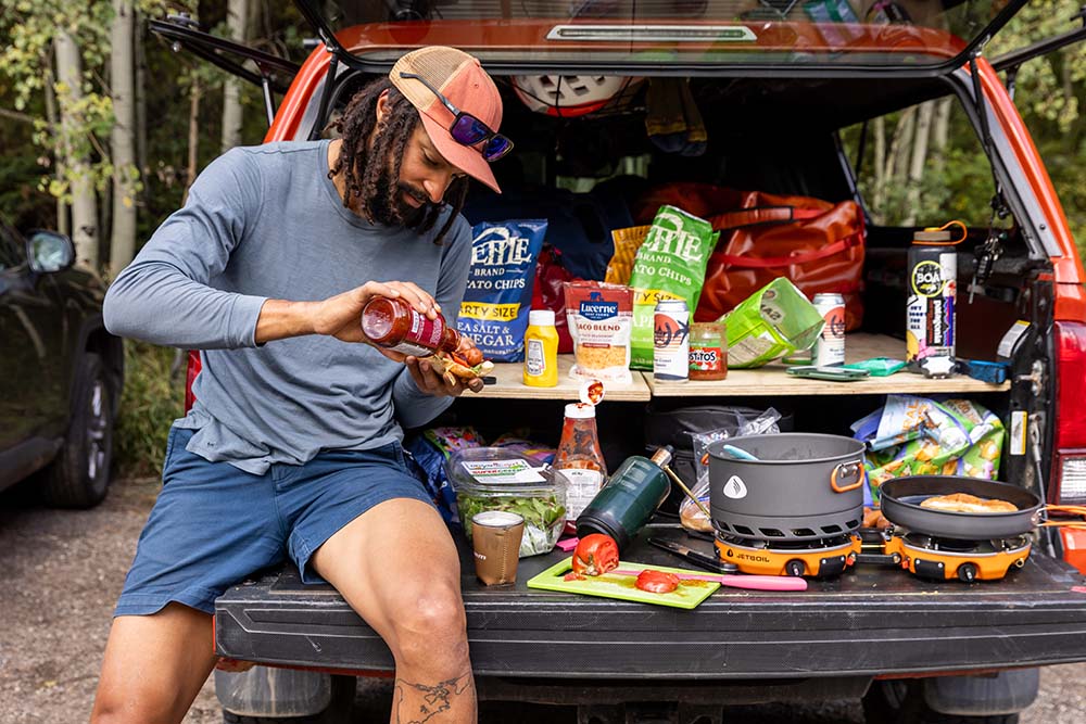 Pouring hot sauce on hot dog cooked with Jetboil Genesis Basecamp System