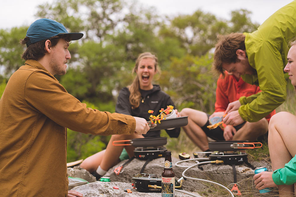 Group of friends enjoying a camping meal cooked on various Jetboil cooking systems