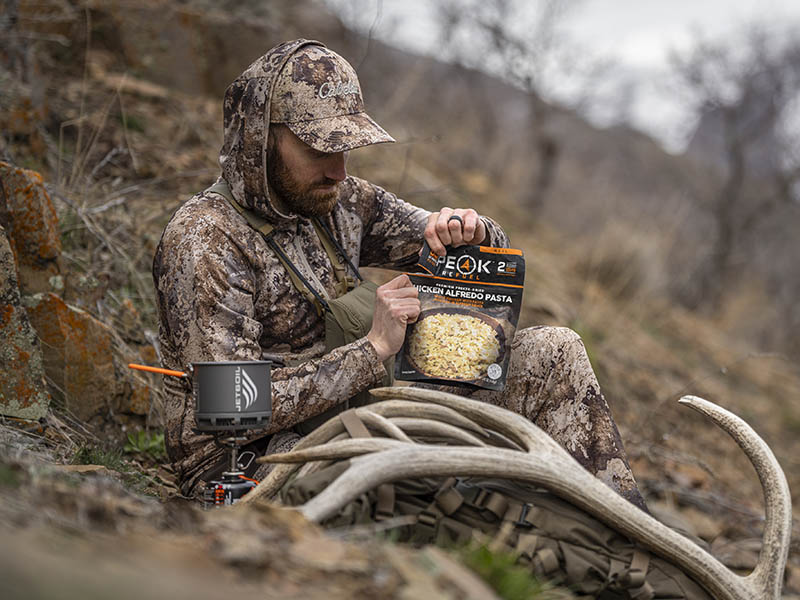 An elk hunter in camo cooks a dehydrated meal in a Jetboil Stash.