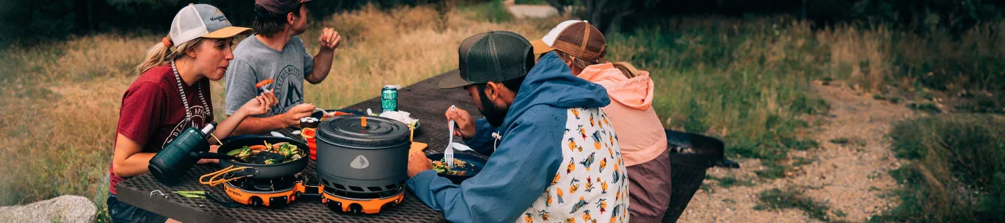 Group of friends at campsite eating a meal cooked on Jetboil Genesis Basecamp System