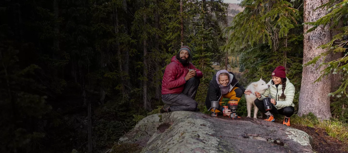 Three backpackers cook and eat on a large boulder.