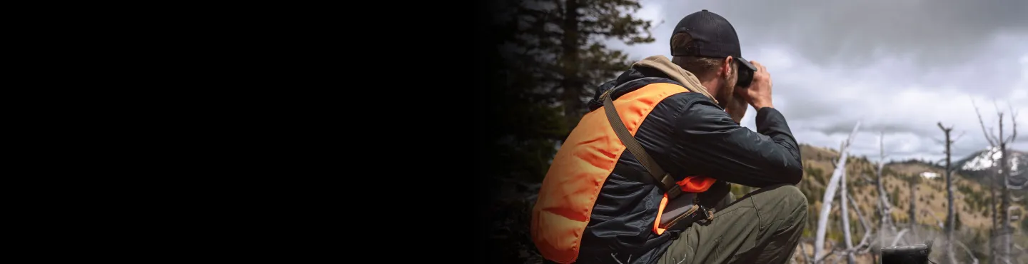 Man in hunting gear looking ahead in distance through binoculars with Jetboil cooking system