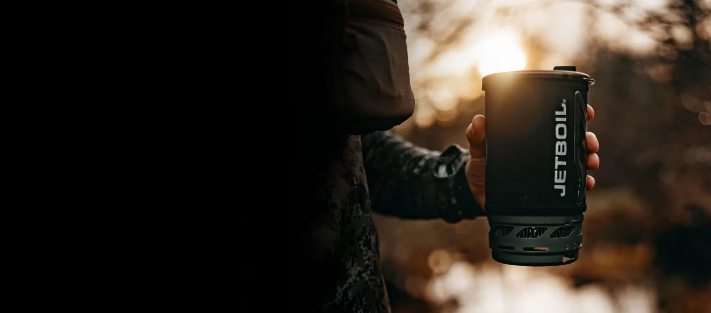 Hunter holding Jetboil Flash cooking system cup in hand outside with sunsetting in background