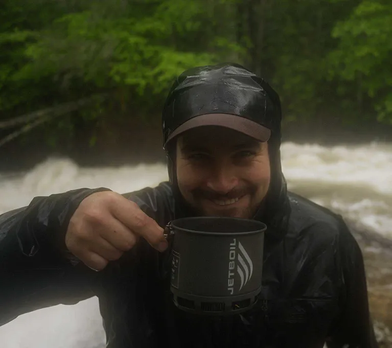Smiling backpacker holding Jetboil Stash cooking system in front of river rapids