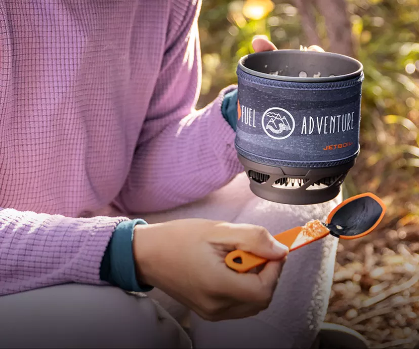 Holding the Jetboil MiniMo Cooking System with a cooked meal inside and TrailWare spoon